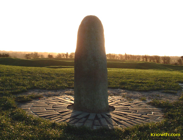 Lia Fáil standing stone on the Hill of Tara, backlit by low sun on a radiating stone pavement.