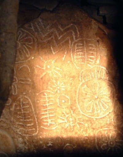 Tall view of equinox sunlight illuminating sun symbols, zigzags and ladder motifs on the Cairn T backstone at Loughcrew.