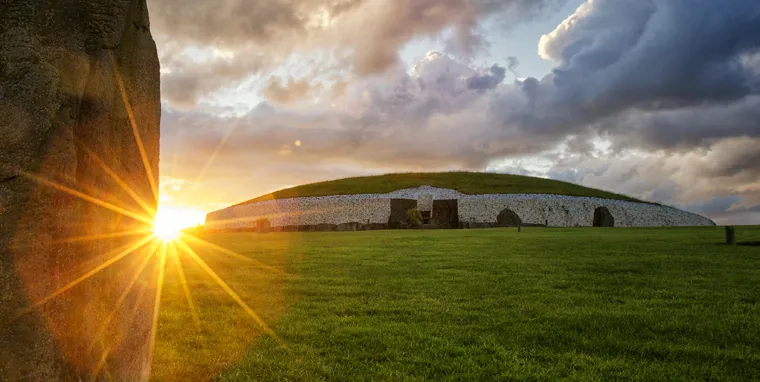 Newgrange at sunset, white quartz wall and entrance framed by a Great Circle orthostat and golden light.