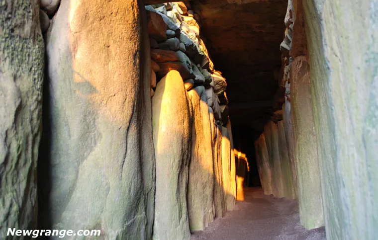 Winter solstice sunlight on upright orthostats in the Newgrange passage beneath corbelled dry-stone walls.